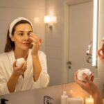 Woman applying night cream to face in bathroom mirror during evening skincare routine